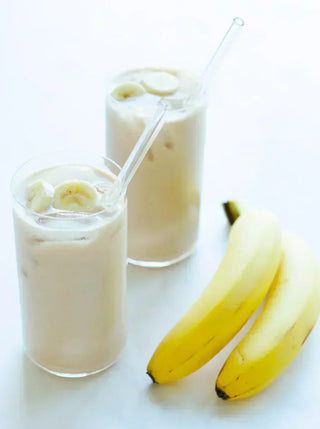two glasses of banana oat milk garnished with banana slices