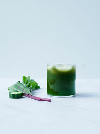 a glass of blush green juice with a kale leaf and slice of cucumber
