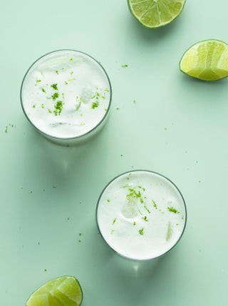 two glasses of creamy coconut limeade with sections of lime on a pale green background