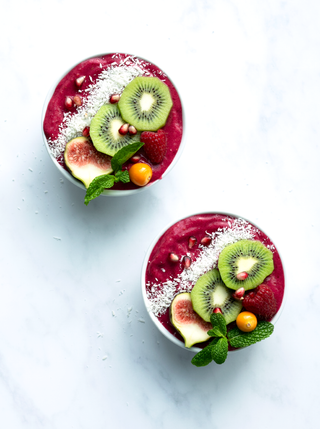Two rich red smoothie bowls topped with sliced kiwi fig and shredded coconut