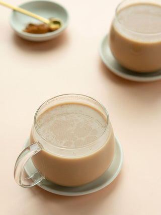 2 glass teacups filled with ginger date milk tea on a light sepia background
