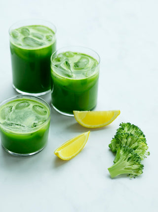 three glasses of green juice with lemon wedges and broccoli tips tips