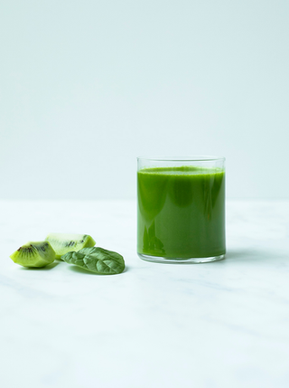 a glass of kiwi green juice with a few spinach leaves