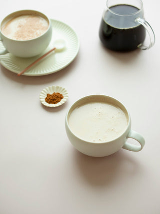 two cups of maple tahini latte with a pitcher of fresh coffee