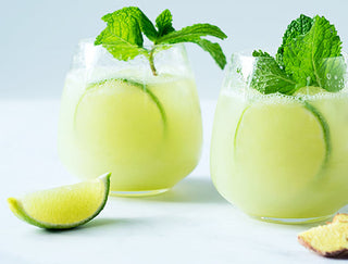 Two glasses filled with a light lime green juice garnished with lime slices and mint