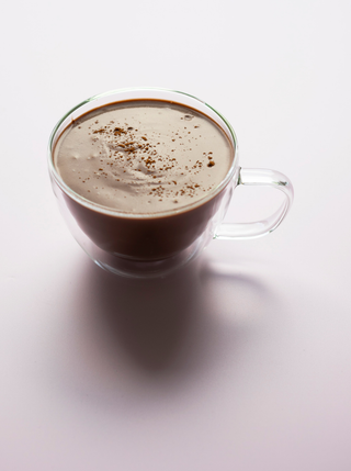 a glass cup with filled with rich choclatey spiced cacao milk on a pale taupe background