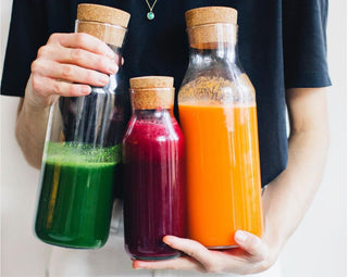 Woman holding 3 large glass bottles of green, red, and orange juice