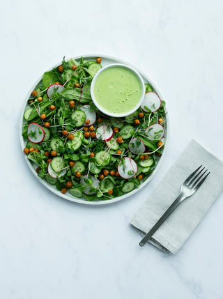 a plate of spring green salad with a cup of nutty green goddess dressing