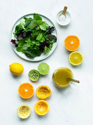 A plate of salad greens jar of dressing with spoon and citrus fruit on a marble surface