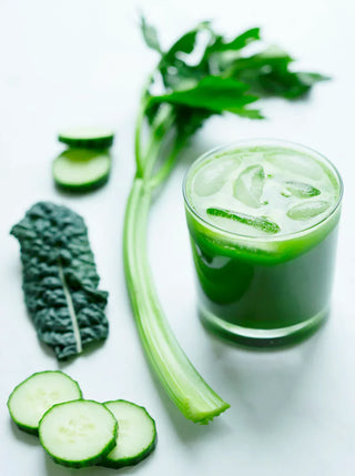 a glass of green juice with ice and ingredients celery cucumber and kale