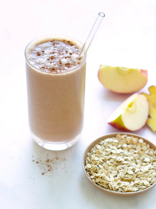 a talll glass of apple pie smoothie, apple pieces and a small bowl of oats