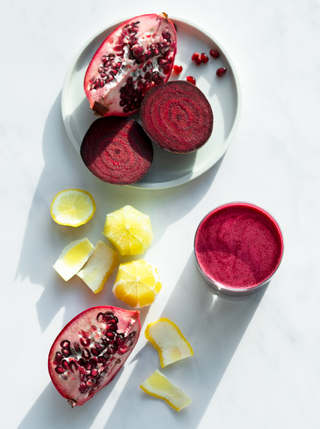 Sliced fresh beets and pomegranate with fresh lemon and a glass filled with beet red beet blitz juice