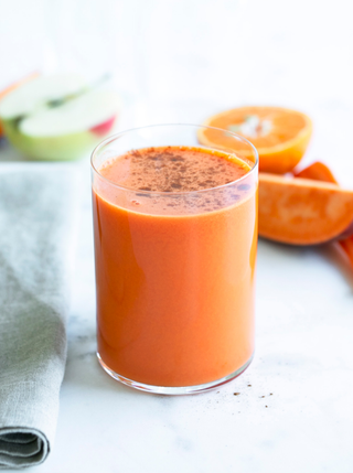 a glass of carrot pumpkin spice juice surrouned by ingredients