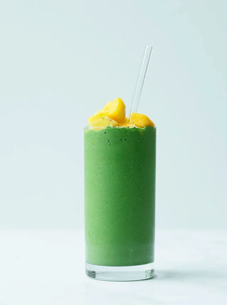a tall glass og green mango recovery smoothie topped with mango pieces