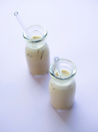 2 small milk bottles filled with lavendar fog milk on a purple background