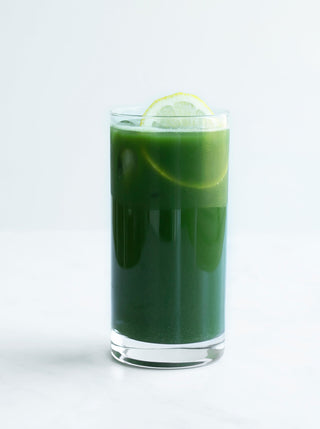 A tall glass of green juice with a slice of lemon