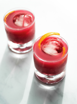Two no-groni mocktails in glass tumblers with  ice and a  sliver of orange peel.