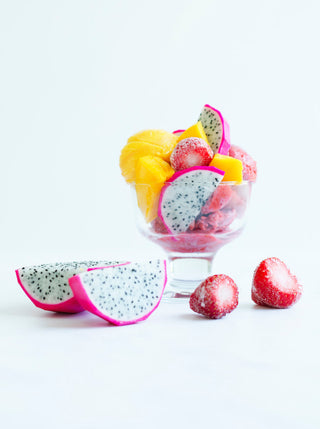 A glass bowl of filled with pieces of pink dragon fruit mango and strawberries