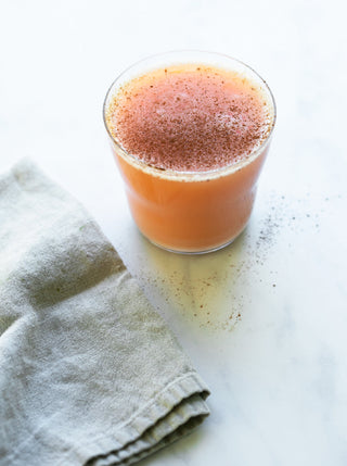 A glass filled with Sweet Potato Spice Juice on a marble counter with a gray linen napkin in the bottom left corner.