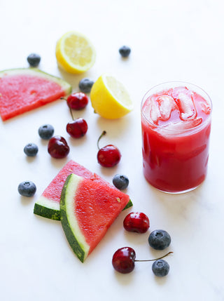 A glass of iced Sweet Watermelon Cherrry juice with ingredients on the side