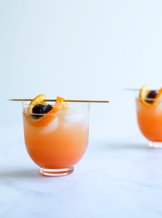 A glass filled with orange juice and ice garnished with orange peel on a skewer