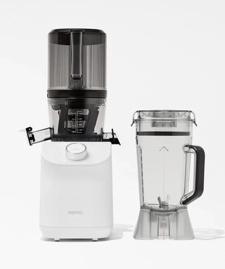 A white Nama juicer with a black top is displayed next to a clear blender pitcher filled with water, both against a plain white background.