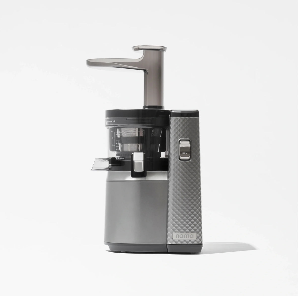 The Nama J1, a modern cold press juicer in silver and black with a transparent container and a textured side panel for enhanced grip, is designed to extract nutrient-rich juices and is displayed against a plain white background.
