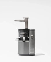 A modern silver and gray juicer with a textured side panel, clear juice container, and vertical feed tube, standing on a plain white background.