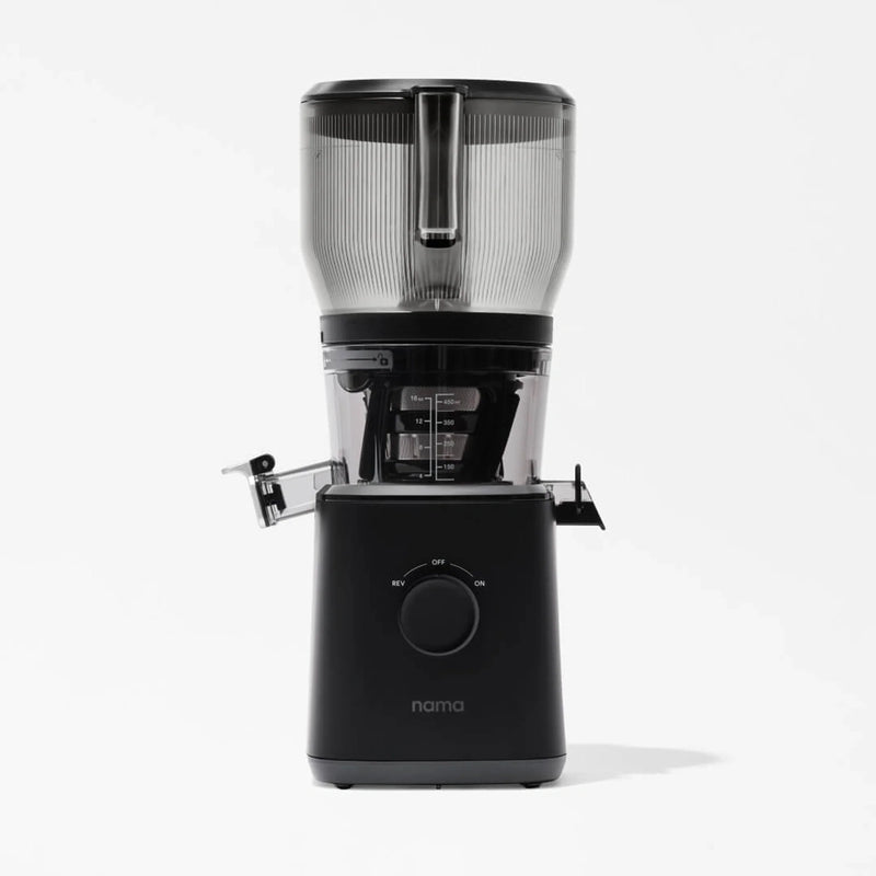 A black Nama J2 XL Cold Press Juicer with a clear container and lid, viewed from the front, sits on a plain white background. This cold press juicer features a round dial and two side spouts for juice and pulp, making it an easy-to-clean juicer that’s both stylish and functional.