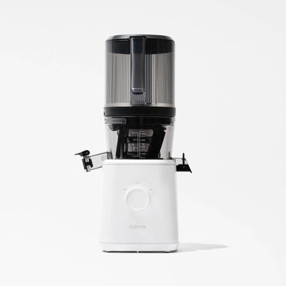 A Nama J2 Cold Press Juicer in white, featuring a transparent black container with a handle and a left-side spout, is photographed against a plain white background. The Nama J2 is engineered for effortless juicing and is recognized for its easy-to-clean design.