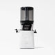 A Nama J2 Cold Press Juicer in white, featuring a transparent black container with a handle and a left-side spout, is photographed against a plain white background. The Nama J2 is engineered for effortless juicing and is recognized for its easy-to-clean design.