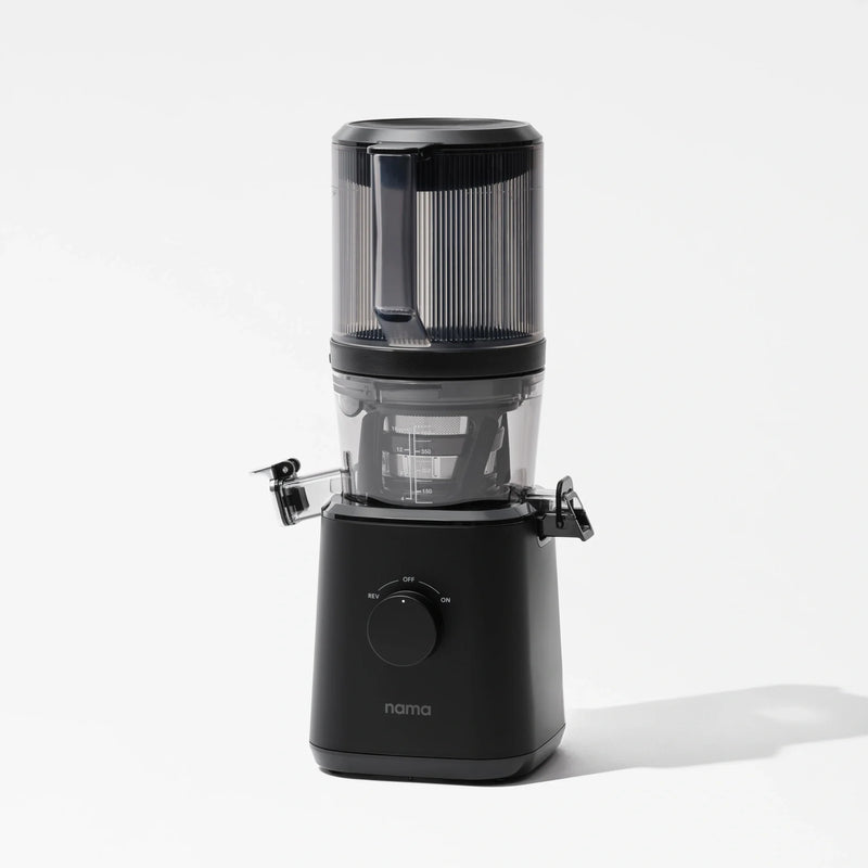 A sleek black Nama J2 juicer featuring a transparent top container and a front-facing control dial stands against a plain white background. The Nama J2 cold press juicer is engineered to provide fresh, nutrient-rich juice and boasts an easy-to-clean design for maximum convenience.