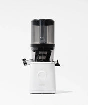 A vertical slow juicer with a transparent upper hopper and a white base labeled nama is shown against a plain white background. The juicer features a spout and a large control dial on the front.