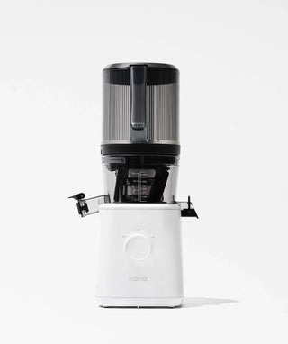 A vertical slow juicer with a transparent upper hopper and a white base labeled nama is shown against a plain white background. The juicer features a spout and a large control dial on the front.