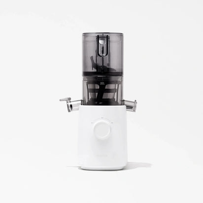 The Nama J3 is a modern cold press juicer featuring a white base, a central dial, and a transparent dark gray container on top, displayed against a plain white background.