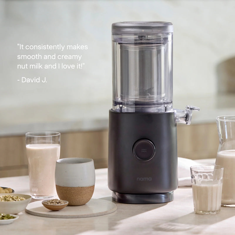 The Nama M1 plant-based milk maker sits on a kitchen counter alongside glasses and a jug of nut milk. A quote on the left reads, “It consistently makes smooth and creamy nut milk and I love it!” – David J. Perfect for creating barista-quality milk at home.