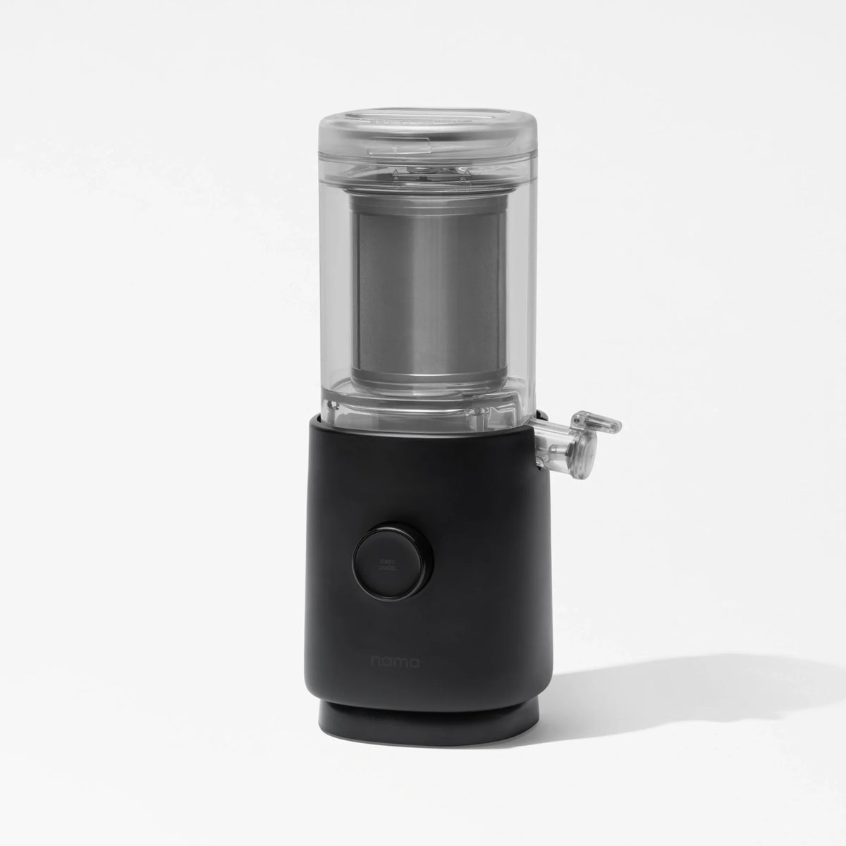 A sleek, black and transparent Nama M1 countertop appliance with a cylindrical glass container on top, a circular control button on the front, and a small side spout is photographed against a white background—perfect for making fresh plant-based nut milk or barista-quality milk at home.