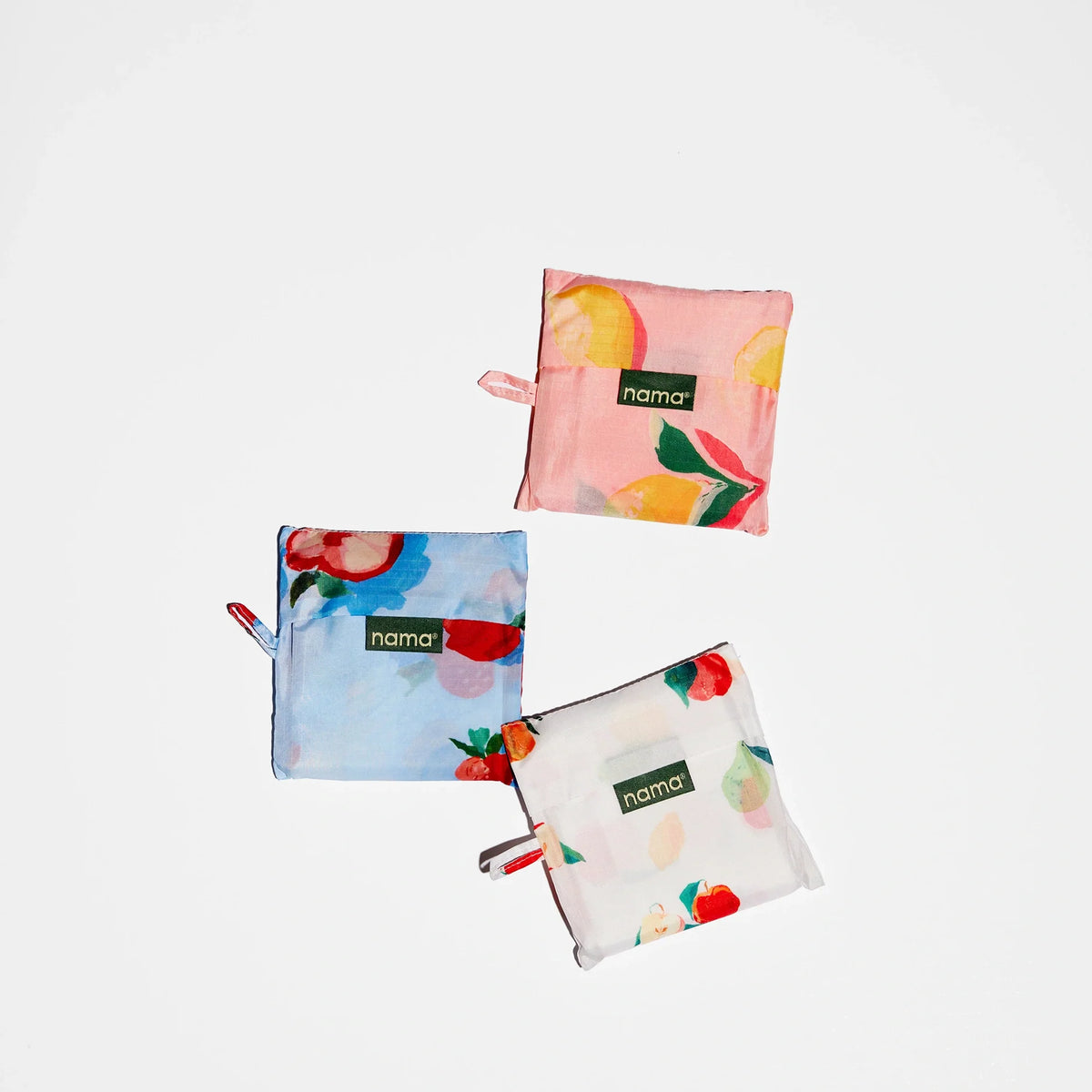 Three vibrant Nama + Baggu Standard Tote Bags, featuring cheerful fruit patterns and a square shape, are displayed on a white background. Ideal as reusable bags for carrying fresh produce, each tote includes a small fabric tag labeled “nama.”.