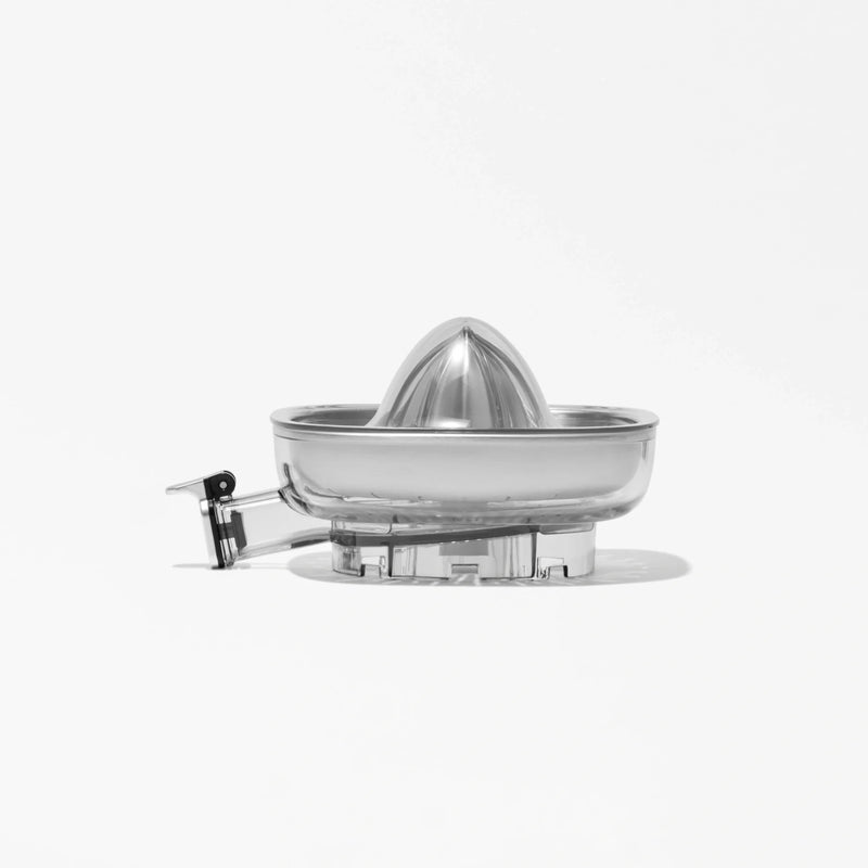 A clear, plastic Citrus Attachment with a reamer and spout is displayed on a white background. The simple and modern design of the Citrus Attachment makes juicing citrus fruits efficient, while shadows fall beneath it.
