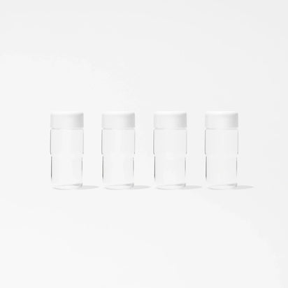 A set of four identical, clear cylindrical glass bottles from the Glass Bottle Set, each topped with a white mason jar lid, are displayed in a straight line on a plain white background. Evenly spaced and matching in design, these bottles are ideal for organized juice storage.