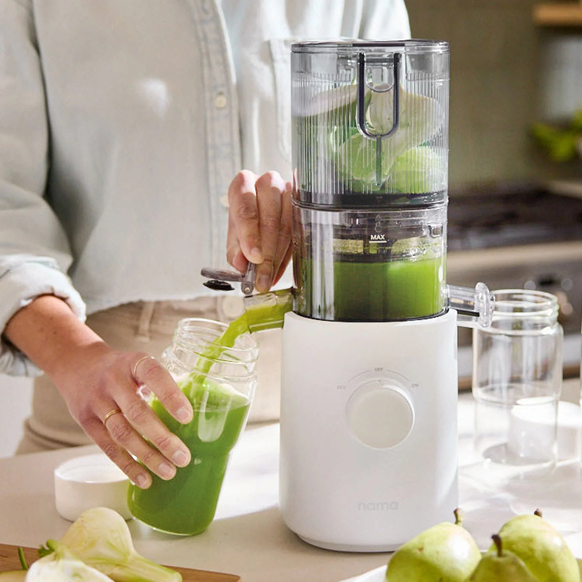 A person uses a white juicer to pour fresh green juice into a jar from the Glass Bottle Set. Whole green apples and another empty glass bottle from the set are on the counter, showcasing versatile options for juice storage. The scene is bright and set in a kitchen.