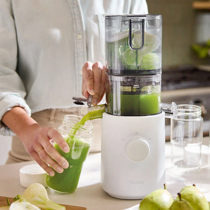 A person uses a white juicer to pour fresh green juice into a jar from the Glass Bottle Set. Whole green apples and another empty glass bottle from the set are on the counter, showcasing versatile options for juice storage. The scene is bright and set in a kitchen.