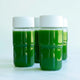 Four clear bottles from the Glass Bottle Set, each filled with green juice and topped with white mason jar lids, are arranged on a light surface. The minimalistic background highlights these bottles, making them ideal for stylish juice storage.