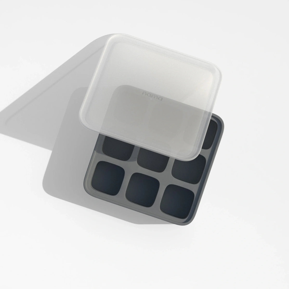 The Ice Cube Tray is made of black silicone and features eight compartments, shown with a translucent lid partially covering it and casting a shadow on a white surface.