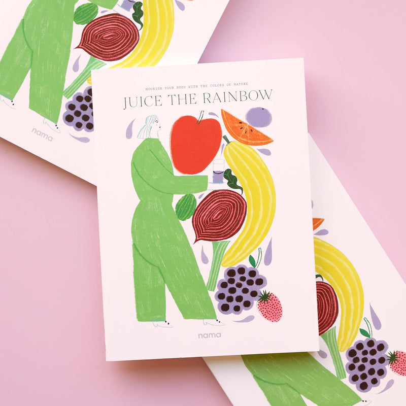 The Juice the Rainbow Book is an illustrated recipe booklet shown on a pink surface, featuring a person in green holding large colorful fruits and vegetables, surrounded by berries and leafy greens—a vibrant celebration of plant-based nutrition.