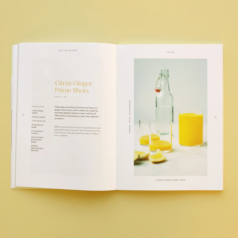 An open copy of the Juice the Rainbow Book rests on a yellow surface, displaying a vibrant citrus ginger drink recipe on the left—ideal for anyone exploring plant-based nutrition. To the right, a photo highlights a glass and bottle filled with yellow juice, alongside lemon wedges and another glass of orange liquid—a mouthwatering inspiration for your next collection of juice recipes.