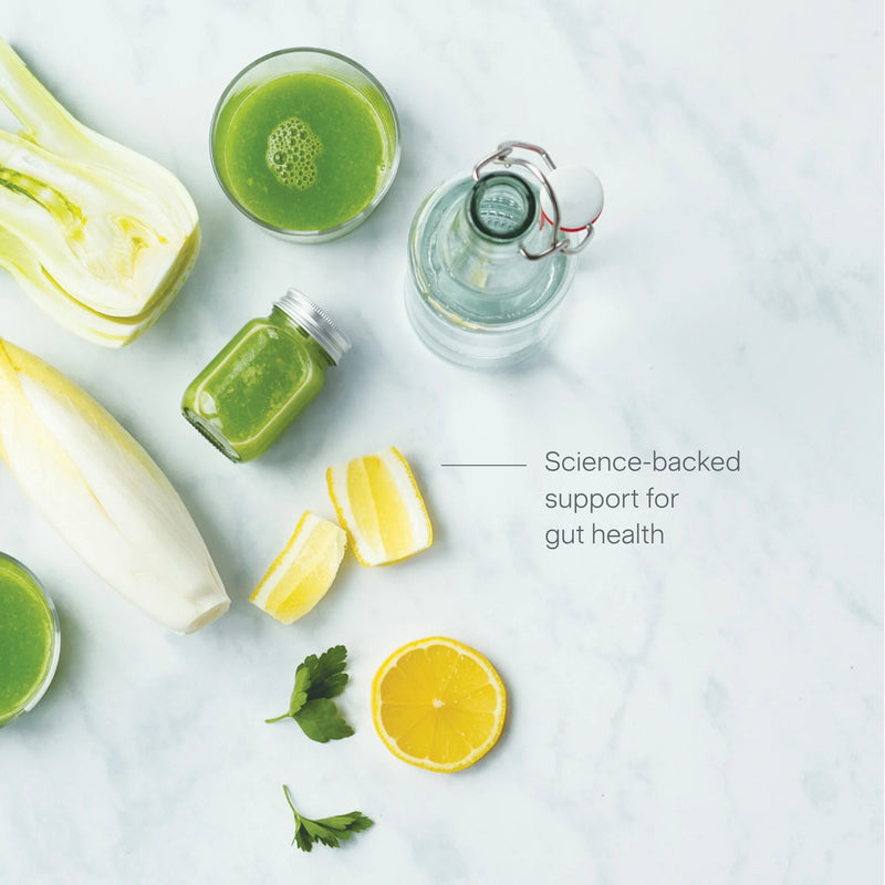 Gut Health green juice in a glass and jar, accompanied by a glass bottle, sliced lemon, fennel, parsley, Belgian endive on a white marble surface with the text “Science-backed support for gut health.”.