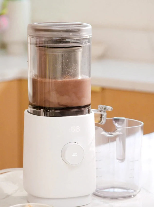A modern white blender with a clear container mixing a chocolate drink on a kitchen counter, with a measuring cup placed beside it.