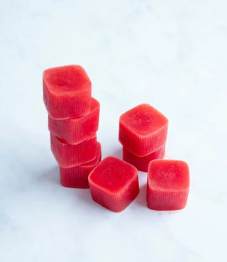 Eight red, square-shaped gummies are stacked and arranged on a white surface. Four are stacked vertically, while the others are placed beside them, showing their textured sides and flat tops.