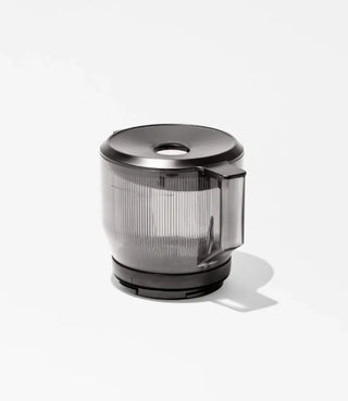 A transparent, ribbed plastic container with a handle and a dark lid, placed on a white surface casting a shadow to the right.